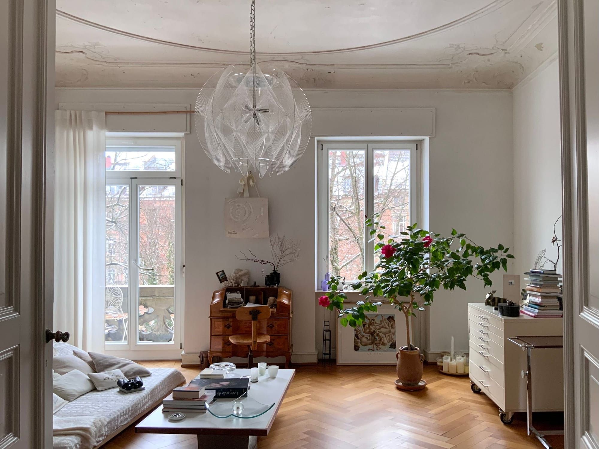 Wohnzimmer mit Stuckdecke, Fischgrätparkett, zwei hohen Fenstern und Pflanzen