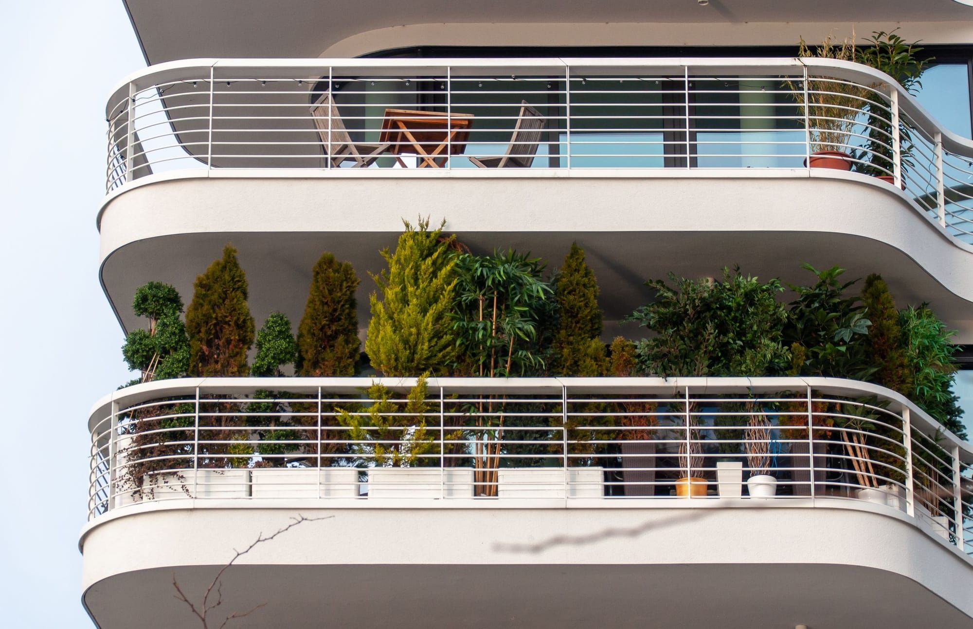 Weiße Balkone mit Pflanzen und Sitzmöbeln an einer modernen Fassade
