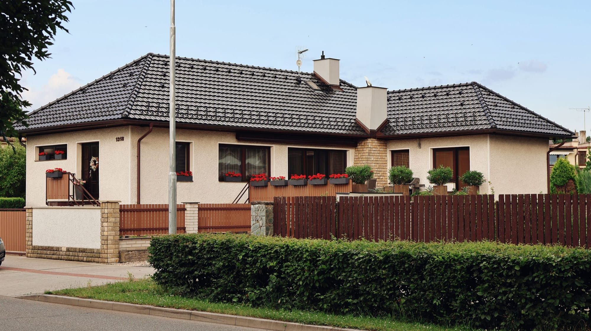 Einfamilienhaus mit Ziegeldach, Hecke und Holzzaun an einer ruhigen Wohnstraße
